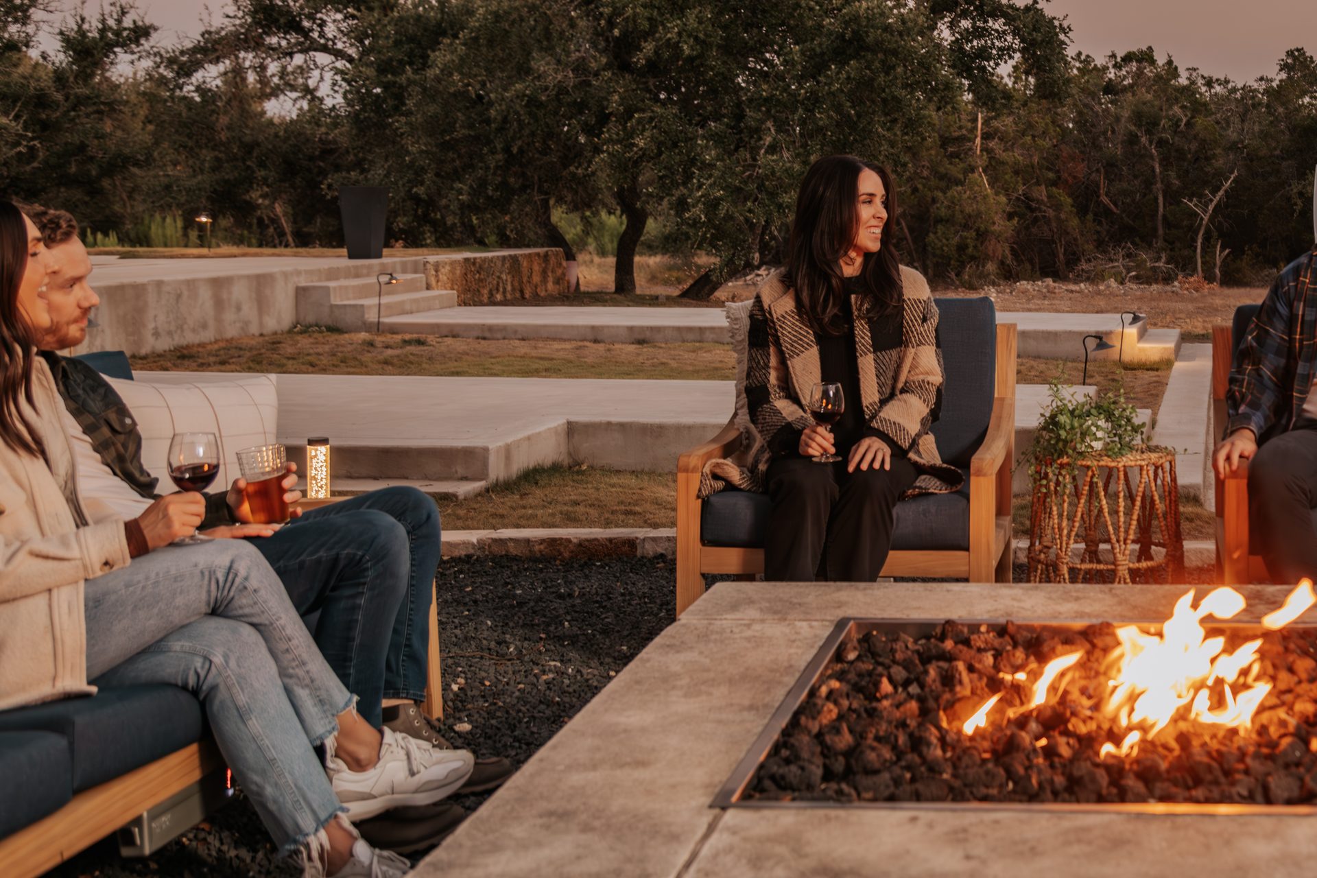 Friends gathered around a fire pit at dusk on Outmore Living Solerno teak seating with heated cushions